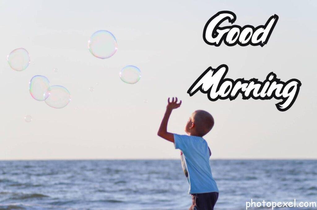 Boy-In-White-T-Shirt-Playing-Bubbles-Near-Body-Of-Water-Under-Grey-Sky-During-Daytime-–-Good-Morning-Images