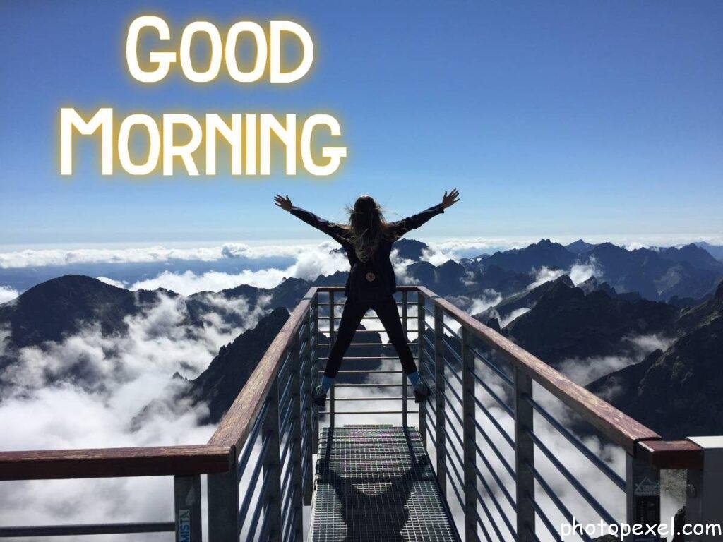 Woman-Standing-On-Handrails-With-Arms-Wide-Open-Facing-The-Mountains-And-Clouds-–-Good-Morning-Images